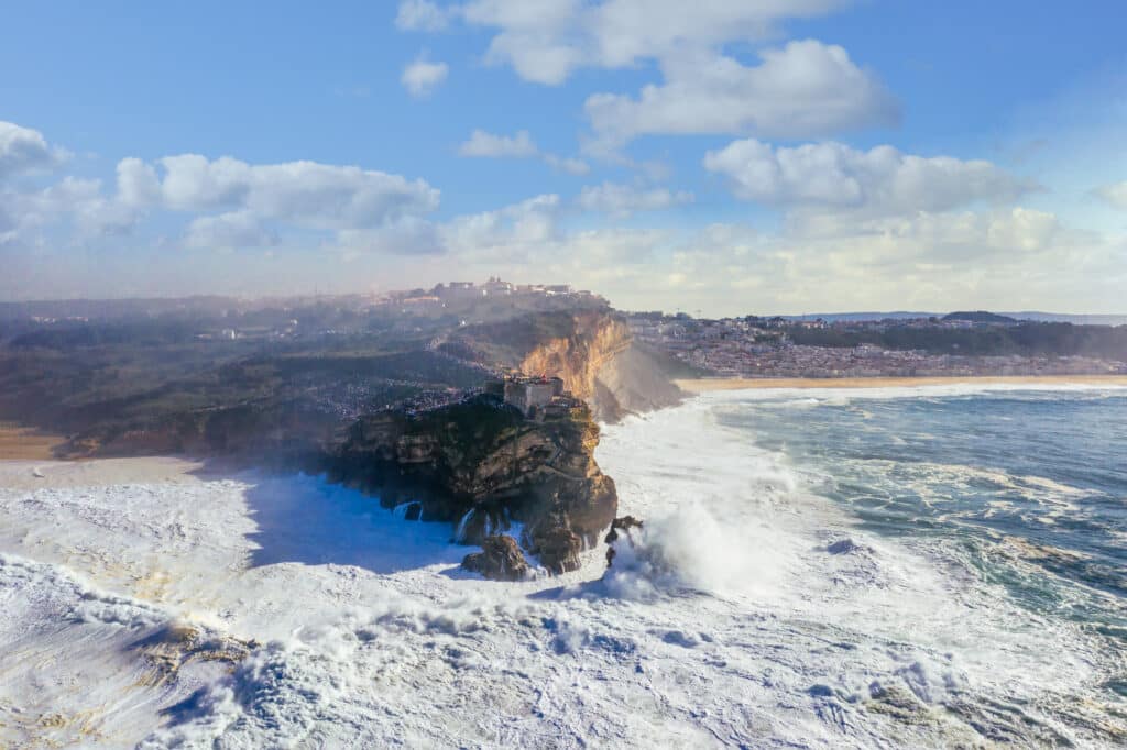 Des spectateurs observent une très grosse houle depuis le fort, avec des jet-skis en attente au pied de la falaise.
